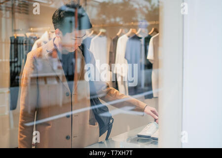 Jeune homme shopping dans le magasin de vêtements. En regardant par la fenêtre Banque D'Images