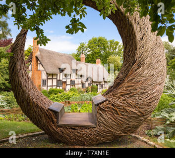 Stratford-upon-Avon, Warwickshire / UK - 18 juin 2018 : Anne Hathaway's Cottage à colombages et son jardin encadrée par une circulaire willow siège. Banque D'Images