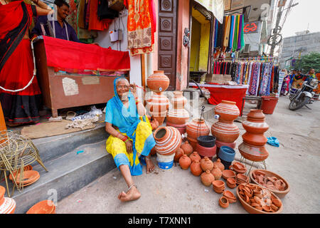 Scène de rue, Chittaranjan Park district, une banlieue de New Delhi : une vieille femme est assise sur le trottoir devant un magasin de vêtements avec un écran de pots en céramique Banque D'Images