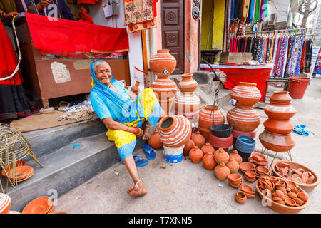 Scène de rue, Chittaranjan Park district, une banlieue de New Delhi : une vieille femme est assise sur le trottoir devant un magasin de vêtements avec un écran de pots en céramique Banque D'Images