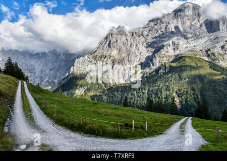 Route de gravier, tourner dans les Alpes Suisses, autour de Grindenwald, avec des pics rocheux entourés de nuages dans l'arrière-plan, et de verts pâturages à l'avant-plan Banque D'Images