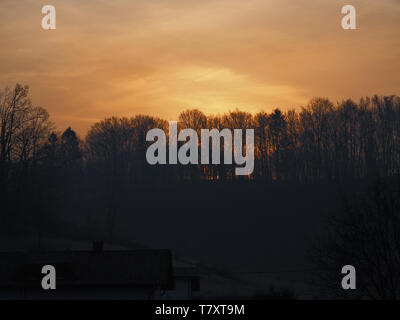 Au début du printemps, le lever du soleil derrière les arbres sur petit village rural en Slovénie Banque D'Images