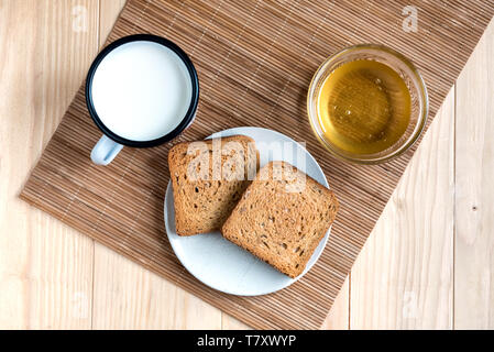 Deux tranches de pain grillé avec de l'étain Mug de lait et pot de miel sur une configuration de table en bois Banque D'Images