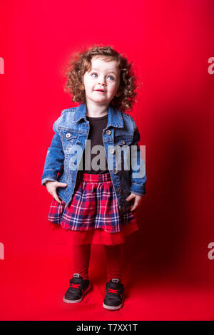 Bébé fille en jupe tartan sur toile rouge Banque D'Images