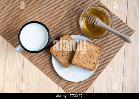 Deux tranches de pain grillé avec de l'étain Mug de lait et pot de miel sur une configuration de table en bois Banque D'Images