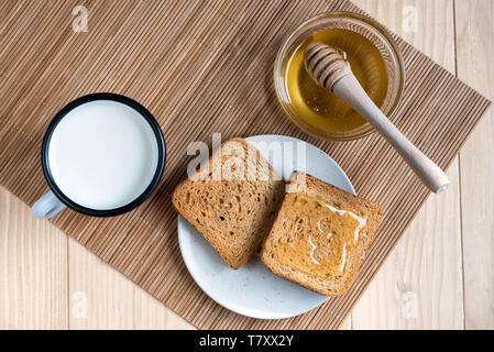 Deux tranches de pain grillé avec de l'étain Mug de lait et pot de miel sur une configuration de table en bois Banque D'Images