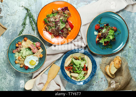 Le bleu et l'une plaque spéciale avec différentes salades : salade de thon, salade de boeuf, salade de calmars, salade de légumes grillés. Belle servant de plats. Fond gris clair. Restaurant menu Banque D'Images