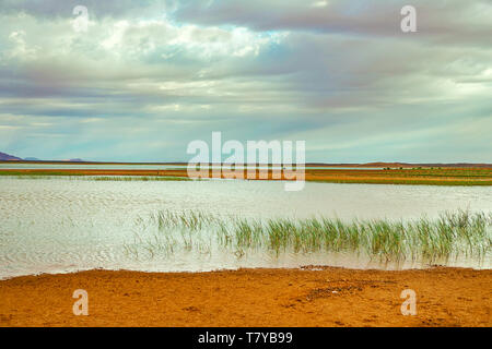 Lake au Maroc à l'aube au pied du désert du Sahara. Les rayons de soleil brillent à travers les nuages. Banque D'Images