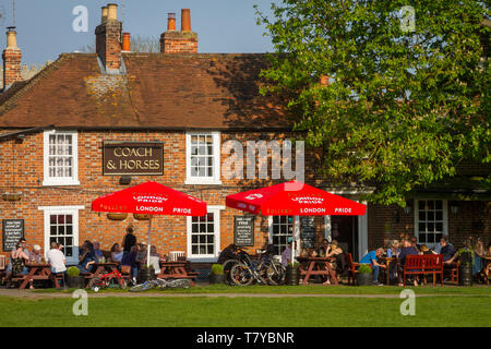 Se détendre dans le soleil du soir sous les parasols rouge vif à l'extérieur de l'entraîneur et les chevaux par la pub, Kinecroft Wallingford par un cheval châtaignier Banque D'Images