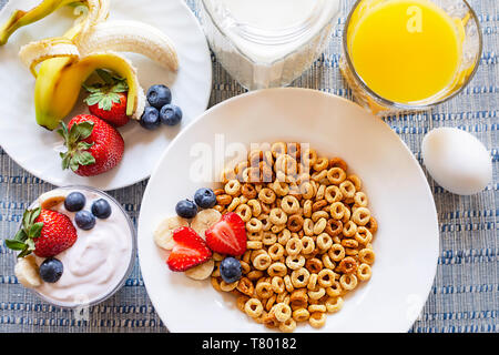 Mise à plat d'un bol de céréales d'avoine avec bananes, fraises, et les bleuets. Plus d'oeuf dur, yogourt, lait, et jus d'orange en vedette Banque D'Images