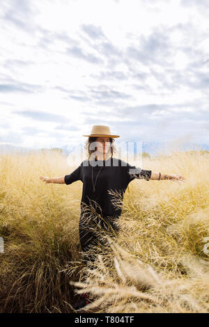 Femme dans la mi-trentaine, posant à bras ouverts avec un chapeau dans un champ d'herbe jaune dans Bodega Septima Winery à Mendoza, Argentine Banque D'Images