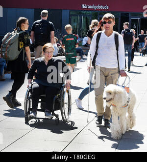 Leipzig, Allemagne. Apr 25, 2019. L'élève aveugle Sebastian Schulze se promène avec son chien-guide, le roi soleil caniche à côté de l'élève handicapé Madeleine Littwin en fauteuil roulant sur le campus de l'Université de Leipzig. Sebastian, maintenant 42, a perdu la vue il y a 14 ans et étudie maintenant les études culturelles. 31 ans, Madeleine, qui a été handicapé depuis la naissance, les études de l'éducation spéciale. Autant de louanges les efforts de l'université d'Etat à l'enseignement et s'engagent pour les étudiants handicapés et n'entraînent pas d'études. Credit : Waltraud Grubitzsch/dpa-Zentralbild/dpa/Alamy Live News Banque D'Images