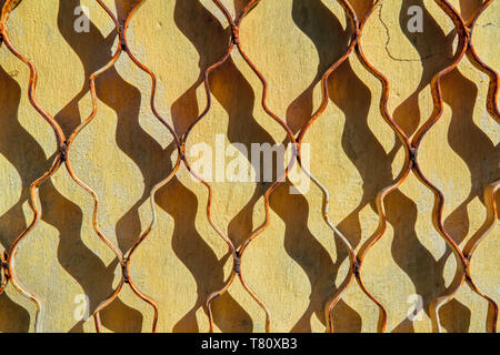 La texture d'un vieux jaune paroi couverte de fissures et grille métallique fermé. Banque D'Images