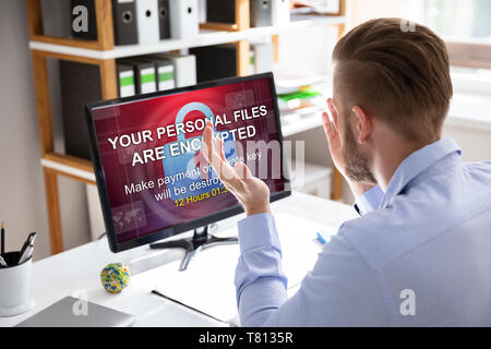 Inquiets Businessman Looking At Computer avec Ransomware mots à l'écran sur le lieu de travail Banque D'Images