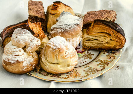 Plaque en porcelaine vintage avec des pièces de différents gâteaux, éclairs, baklava traditionnel arménien et 'cookies' Gata de pâte feuilletée sur une nappe blanche Banque D'Images