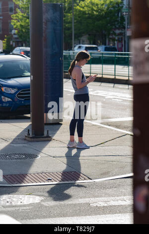 Portrait de la rue pris à Philadelphie en Pennsylvanie, d'une jeune femme en vêtements de sport à la recherche à son téléphone par la route Banque D'Images
