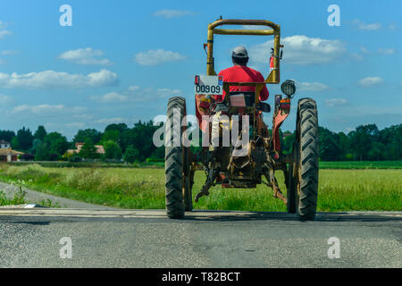 Une vue arrière d'un paysan français dans un tracteur avec pneus minces, traversée d'une ligne de chemin de fer. Près de Gaillac, Occitanie, France. Banque D'Images