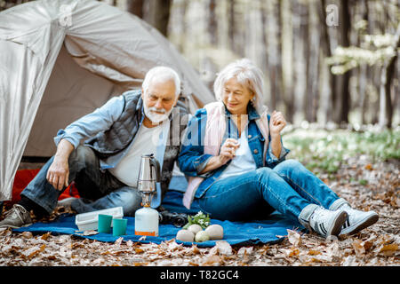 Senior couple sitting ensemble au camping faire un pique-nique avec du café dans la forêt Banque D'Images