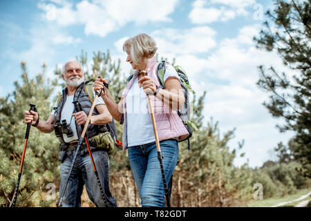 Happy senior couple trekking randonnée avec des bâtons et sacs à dos à la jeune forêt de pins. Profiter de la nature, passer un bon moment sur leur retraite Banque D'Images