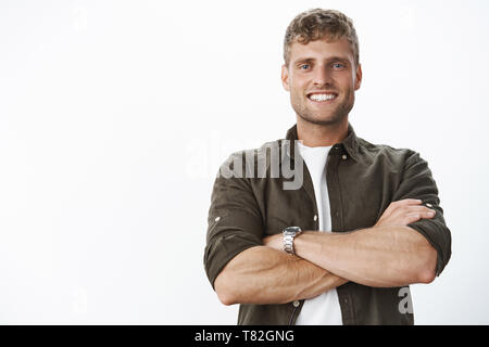 Solide et masculine de bon à l'homme blanc avec un sourire parfait et les yeux bleus, les mains contre les corps en confiant et sûr de poser, satisfait et Banque D'Images