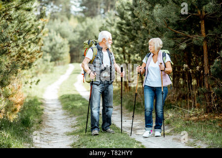 Happy senior couple trekking randonnée avec des bâtons et sacs à dos à la jeune forêt de pins. Profiter de la nature, passer un bon moment sur leur retraite Banque D'Images