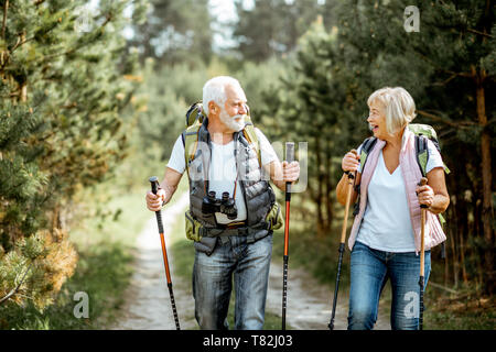 Happy senior couple trekking randonnée avec des bâtons et sacs à dos à la jeune forêt de pins. Profiter de la nature, passer un bon moment sur leur retraite Banque D'Images