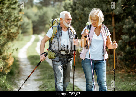 Happy senior couple trekking randonnée avec des bâtons et sacs à dos à la jeune forêt de pins. Profiter de la nature, passer un bon moment sur leur retraite Banque D'Images