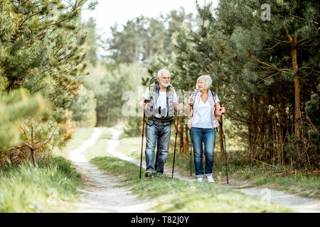 Happy senior couple trekking randonnée avec des bâtons et sacs à dos à la jeune forêt de pins. Profiter de la nature, passer un bon moment sur leur retraite Banque D'Images