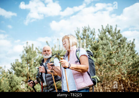 Happy senior couple trekking randonnée avec des bâtons et sacs à dos à la jeune forêt de pins. Profiter de la nature, passer un bon moment sur leur retraite Banque D'Images