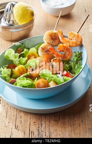 Salade de fruits de mer délicieux grillé épicé avec démarreur et langoustines pétoncles frais sur des brochettes en bois servi avec croûtons sautés croquants Banque D'Images