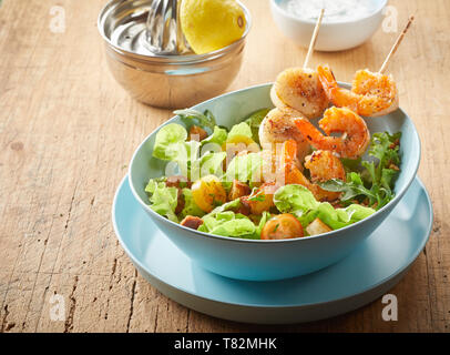 Apéritif de fruits de mer gastronomique aux scampi et pétoncles grillés sur des brochettes et servi sur une salade verte avec croûtons frits dans un close up high angle v Banque D'Images