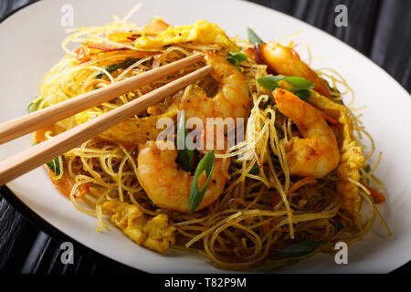 Nouilles de riz frit épicé avec de la saucisse, les crevettes et les légumes sur une assiette sur la table horizontale. Banque D'Images