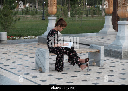 Une jeune femme ouzbèke lit un livre au complexe du Monument de la mère qui pleure en l'honneur des mères des soldats ouzbeks morts pendant la seconde Guerre mondiale dans la ville de Termez capitale de Surxondaryo ou région de Surkhandarya dans le sud de l'Ouzbékistan en Ouzbékistan Banque D'Images