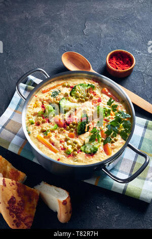 Soupe de Brocoli garni de persil frais, de fromage cheddar râpé, les pois verts et les légumes dans un chaudron sur une table de béton gris avec cuillère en bois Banque D'Images