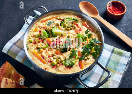 Close-up de soupe Brocoli garni de persil frais, de fromage cheddar râpé, les pois verts et les légumes dans un chaudron sur une table de béton gris avec Banque D'Images
