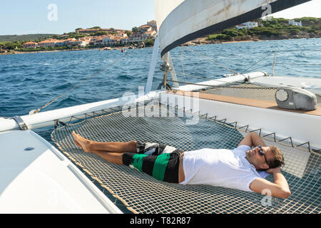 L'homme sportif détente sur un catamaran de luxe à voile. Banque D'Images