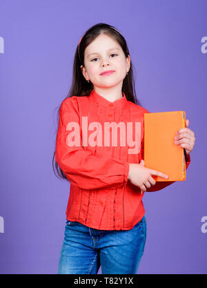 Confiant dans sa connaissance. Adorable petite fille tenant livre avec couvercle orange. Enfant mignon petit livre avec la connaissance dans les mains. Connaissances et compétences. Jour des connaissances ou le 1 septembre, l'espace de copie. Banque D'Images