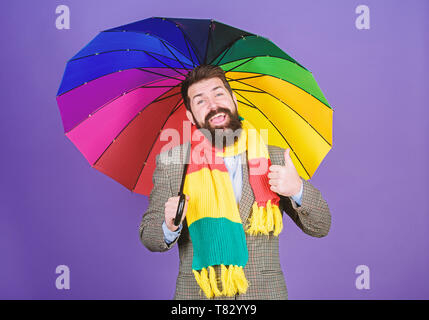 Il aime la pluie. Bearded man giving Thumbs up geste de la main à la pluie la météo. Hipster holding umbrella colorés. Rain man. Le parapluie coloré ne manque jamais d'attirer le regard. Banque D'Images