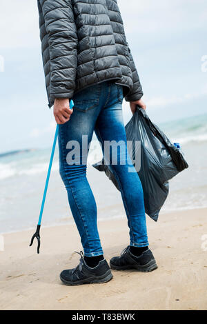 Libre d'un homme de race blanche, vu de derrière, la collecte des déchets avec une corbeille grabber stick, sur une plage solitaire, comme une action pour nettoyer l'envi naturel Banque D'Images