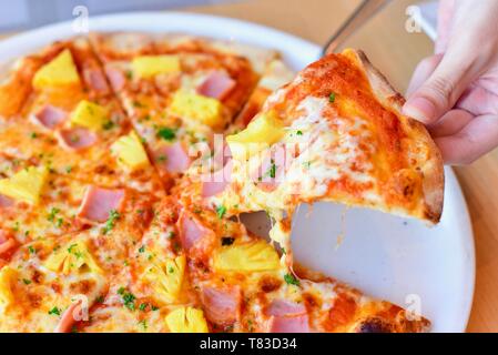 La prise d'une tranche de pizza hawaïenne Banque D'Images