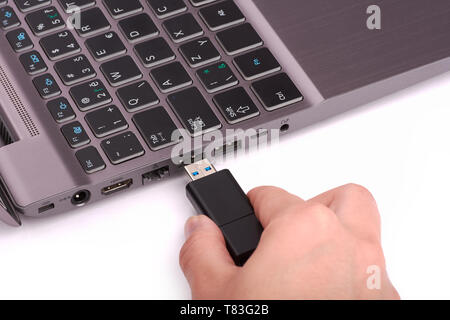 La main d'une jeune femme se connecte un lecteur flash USB à un port dans un ordinateur portable avec un clavier noir. Isolé sur fond blanc. Banque D'Images