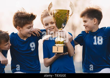 Les garçons de l'équipe sports célébrant la victoire. Des enfants heureux holding golden trophy. L'équipe de football pour enfants sensibilisation des vainqueurs de coupe. Succès sportifs pour la jeunesse Banque D'Images