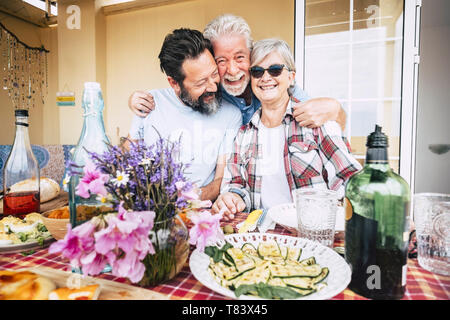 Les personnes âgées de la famille heureuse senior woman hugging et s'amuser devant une table pleine de nourriture et boissons prêtes à célébrer tous ensemble je Banque D'Images