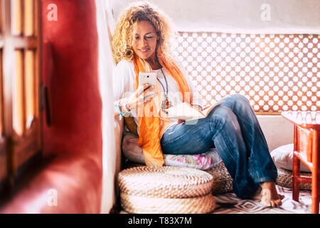 La mode à la mode belle jeune femme les gens à la maison assis et l'utilisation mobile phone at home - vêtements de style hippie et maisons colorées - femelle et techno Banque D'Images