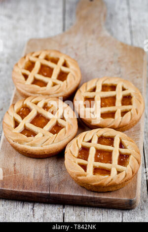 Tartes fraîchement cuit au four avec de la marmelade ou confiture d'abricot sur remplissage sur la planche à découper sur fond de table en bois rustique. Banque D'Images