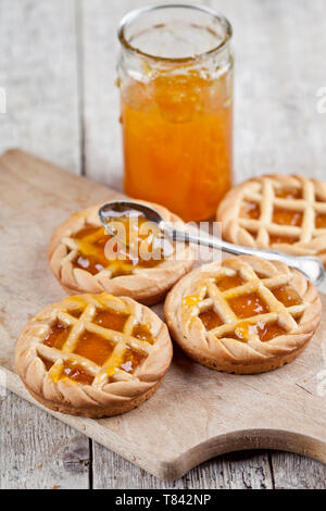 Tartes fraîchement cuit au four avec de la marmelade d'abricots et de remplissage dans un bocal en verre sur une planche à découper sur fond de table en bois rustique. Banque D'Images