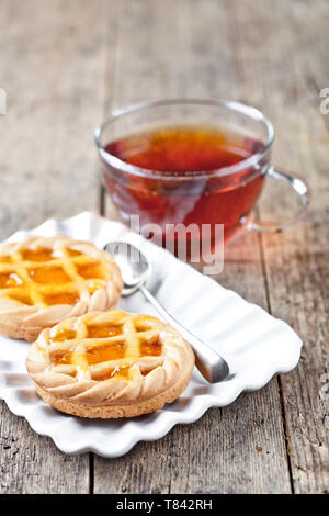 Tartes fraîchement cuit au four avec de la marmelade ou confiture d'abricot garniture sur plaque en céramique blanche et une tasse de thé sur la table rustique en bois, arrière-plan. Banque D'Images