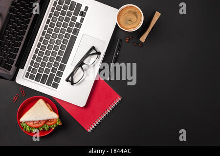 Bureau noir élégant bureau avec ordinateur portable, tasse de café et un sandwich pour le déjeuner. Top View with copy space Banque D'Images