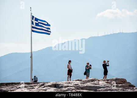 Colline de l'Acropole drapeau grec flottant touristes surplombant la ville Athènes Grèce | ATHÈNES, Grèce — Un drapeau grec flotte de manière proéminente au sommet de l'Acropole, l'ancienne citadelle surplombant la ville étendue d'Athènes. Les touristes se rassemblent sur le sommet rocheux, certains s'arrêtant pour photographier les vues panoramiques de la capitale grecque en contrebas. L'Acropole, site du patrimoine mondial de l'UNESCO et symbole durable de la civilisation grecque antique, offre des perspectives étendues sur le bassin de l'Attique. Banque D'Images