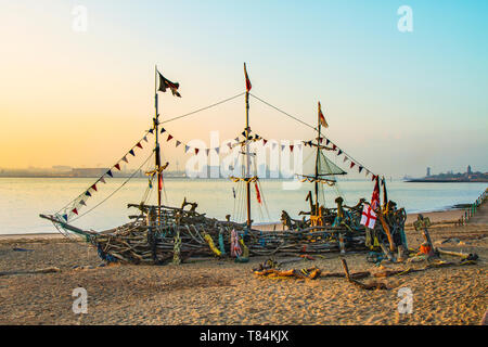 Bateau pirate lever du soleil sur la rivière Mersey, centre-ville, sculpture en bois, quais et port. Le Black Pearl est une œuvre interactive en bois flotté, créée et entretenue par un petit groupe de pirates passionnés sur la rive de New Brighton. Une réplique d'un homme de guerre pirate à trois mâts, il est presque entièrement construit à partir de matériaux récupérés, de la ferraille, des déchets, de l'élimination, de la substance, Épave, équipement, matière première, œuvres d'art en bois flotté sur la plage de Liverpool Merseyside. Banque D'Images